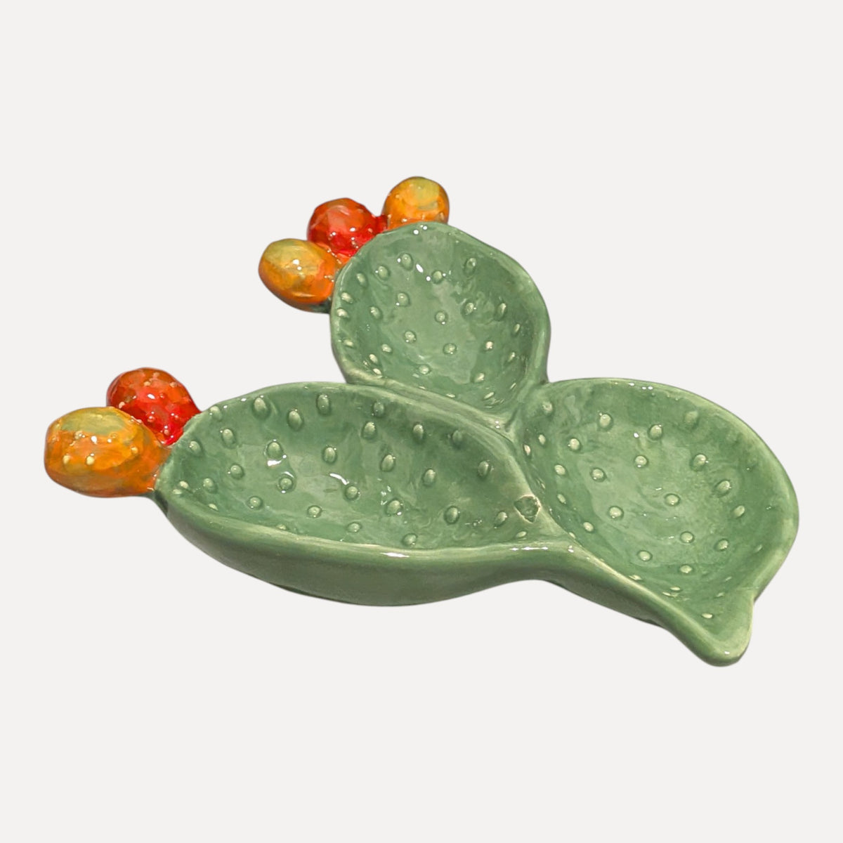 A ceramic cactus-shaped dish in light green with raised textured dots and small orange-red berries, shown on a plain light gray background.