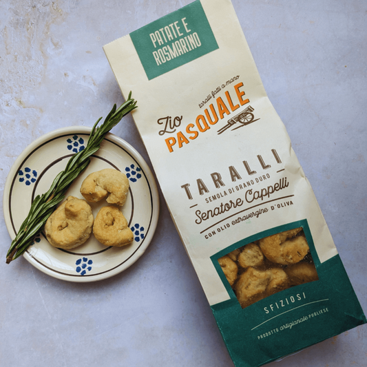 A packet of Taralli with a ceramic plate of taralli and a rosemary stalk on a light background