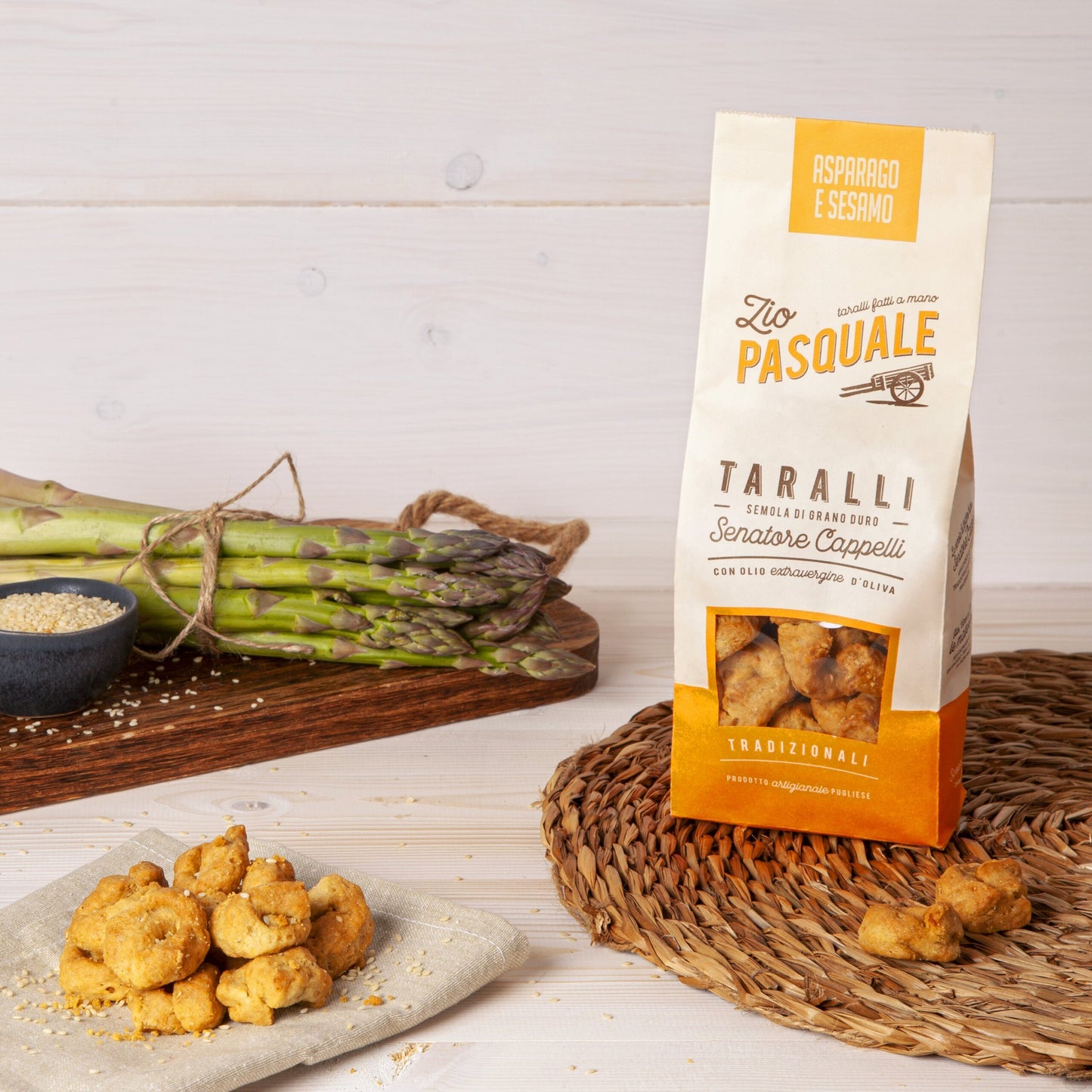 A packet of taralli on a placemat with a bundle of asparagus in the bacground
