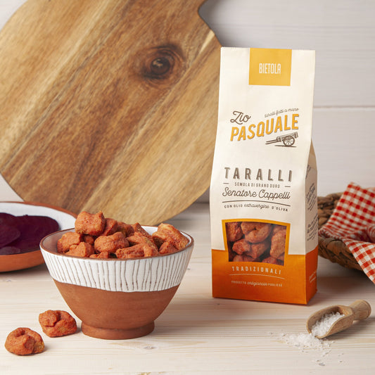 Taralli snacks in a bowl with a box of Zio Pasquale Taralli on a wooden surface.