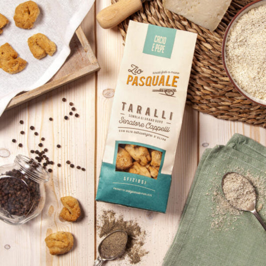 A packet of taralli on a wooden table with whole and ground pepper, placemat and kitchen towel