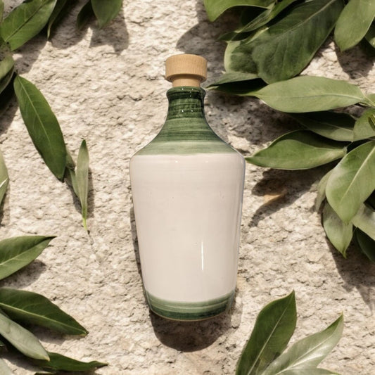 ceramic bottle in white & green on a cement surface with olive tree leaves scattered around