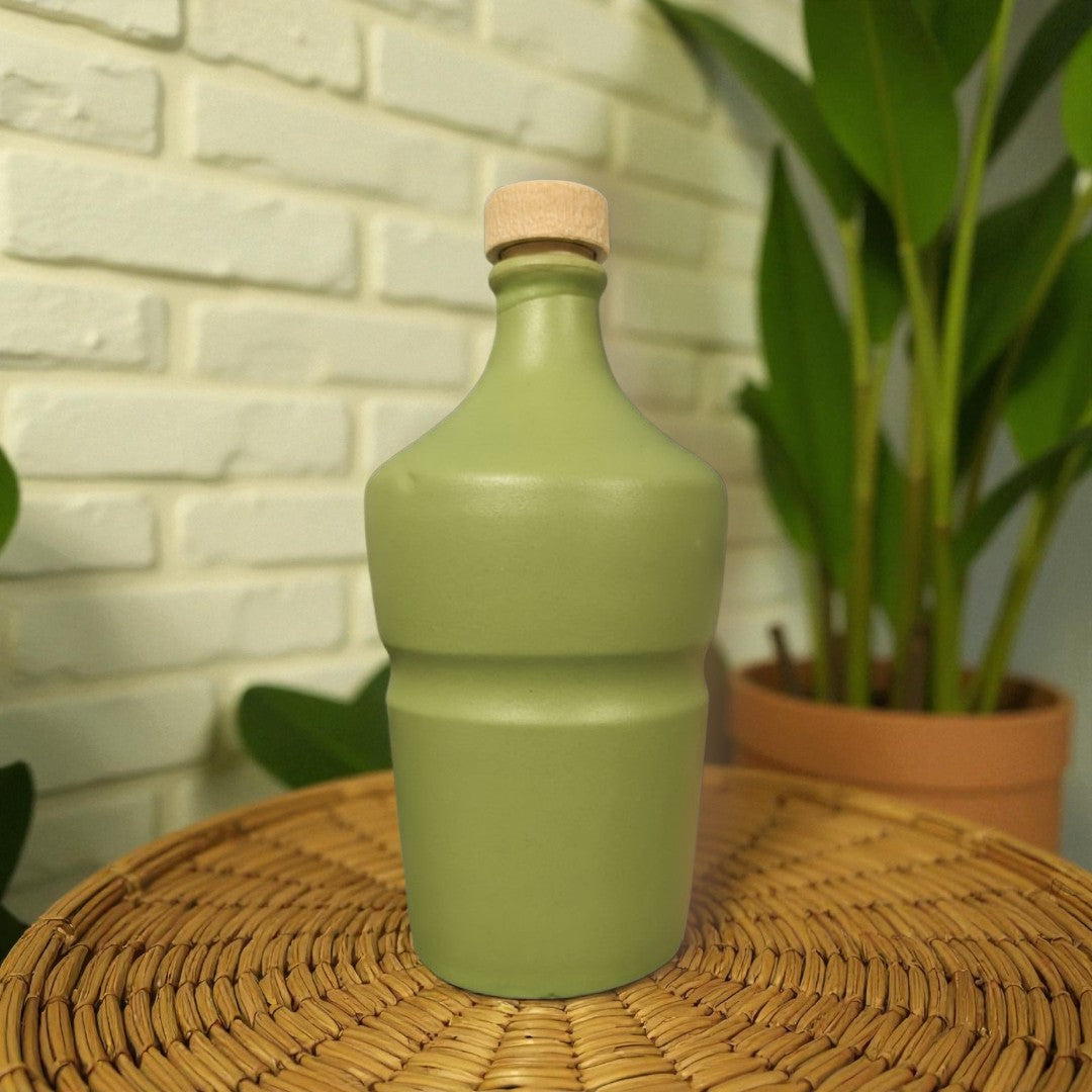 Green ceramic bottle with cork lid on a wicker table with a brick wall and plant in the background