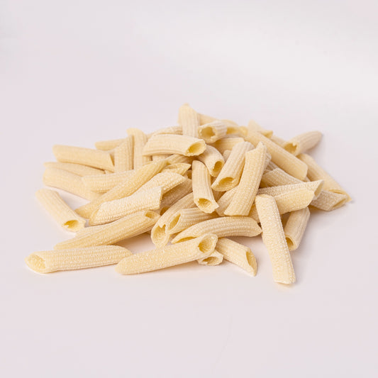 Pile of uncooked penne pasta on a light gray background