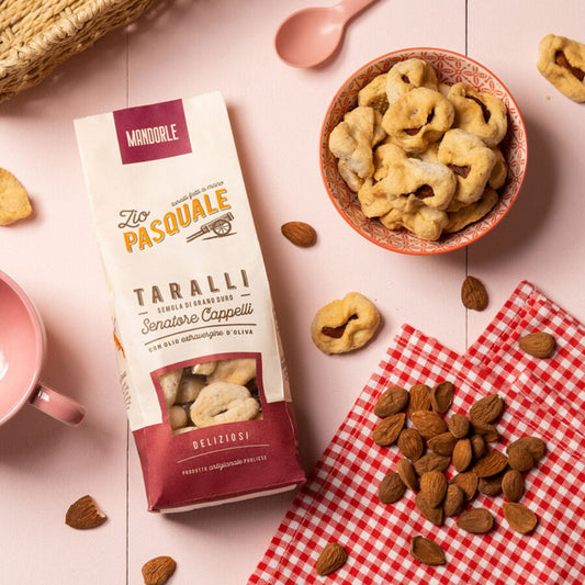 A packet of Zio Pasquale Taralli with a bowl of Taralli, almonds, and a pink spoon on a checkered cloth.