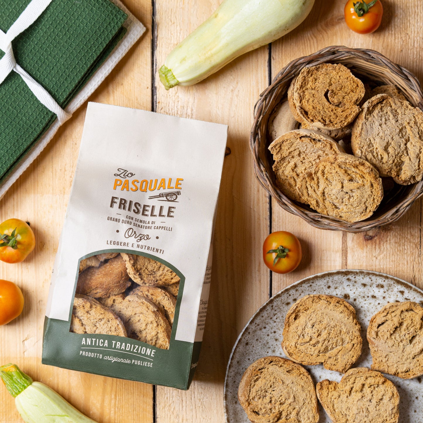 A packet of friselle on a wooden table with vegetables, kitchen mats and plates