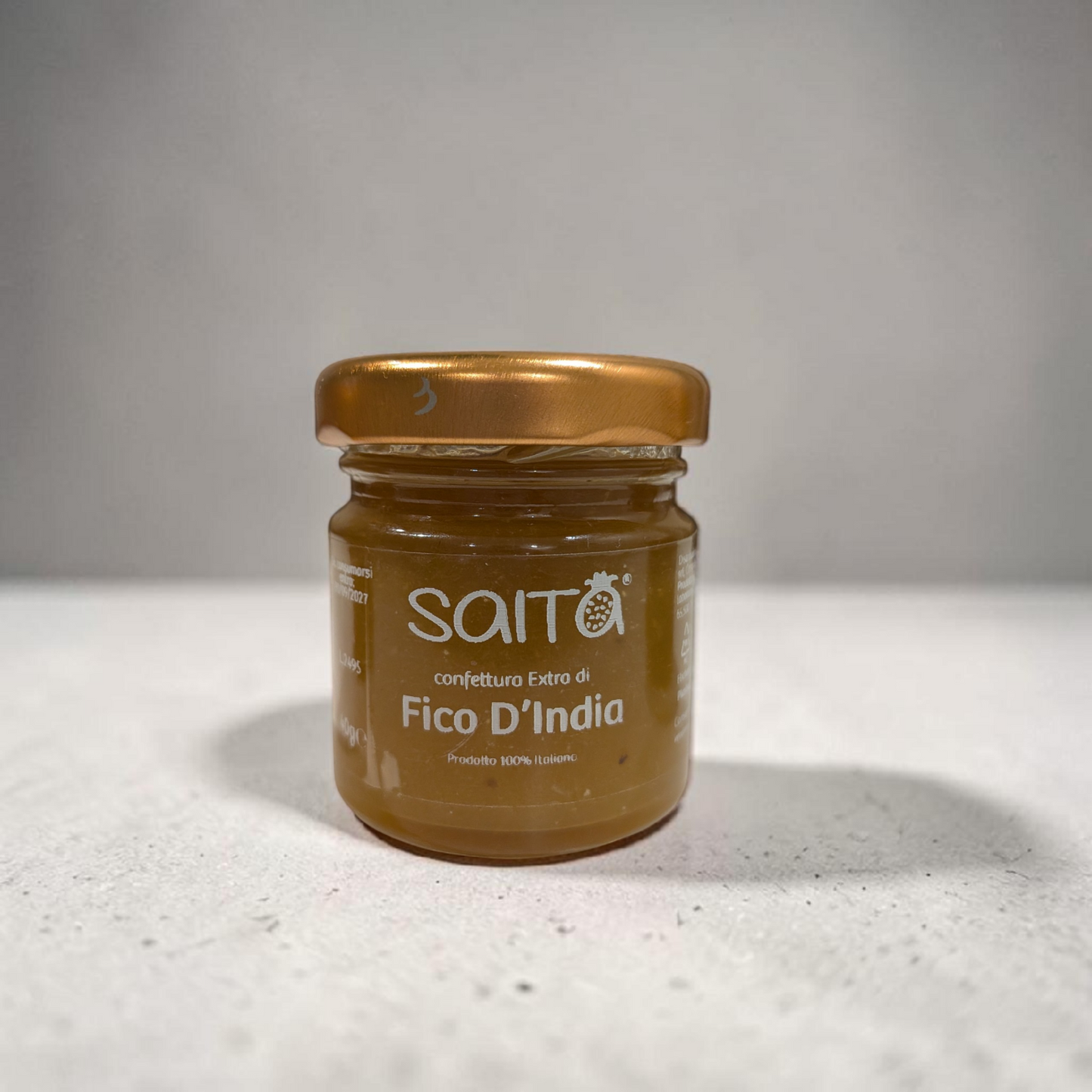 Jar of Saito Fico D'India jam on a white surface with a gray background