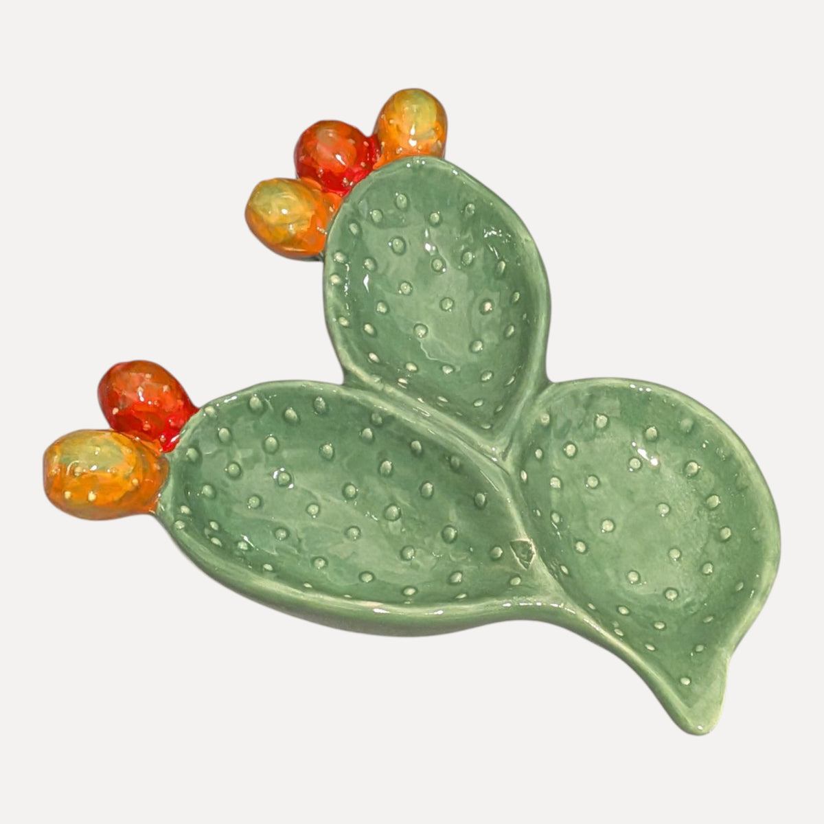 A ceramic cactus-shaped dish in light green with raised dotted texture and small orange and yellow faux prickly pear accents, shown on a plain light gray background.