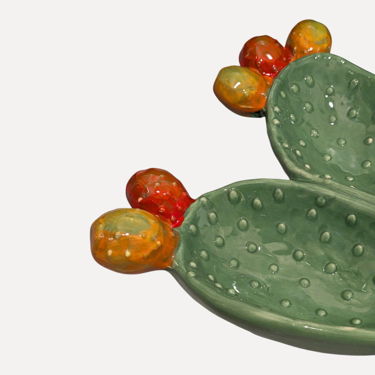 A ceramic cactus-shaped dish with textured green pads and glossy orange-red and yellow-orange fruits, photographed on a clean white background.