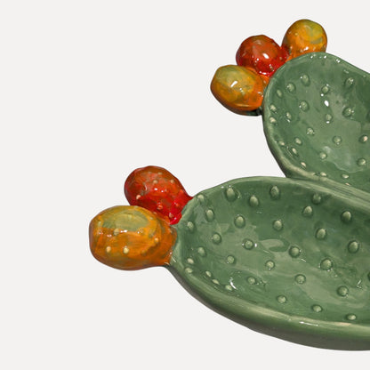 A ceramic cactus-shaped dish with textured green pads and glossy orange-red and yellow-orange fruits, photographed on a clean white background.