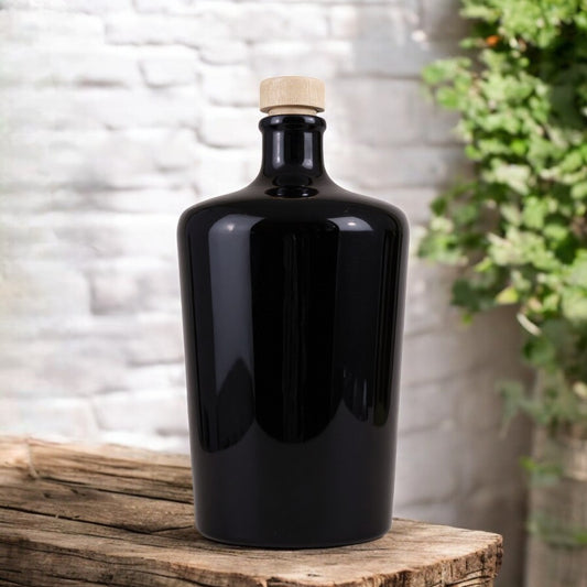 Black ceramic bottle with a cork on a wooden surface with a white brick wall and plants in the background