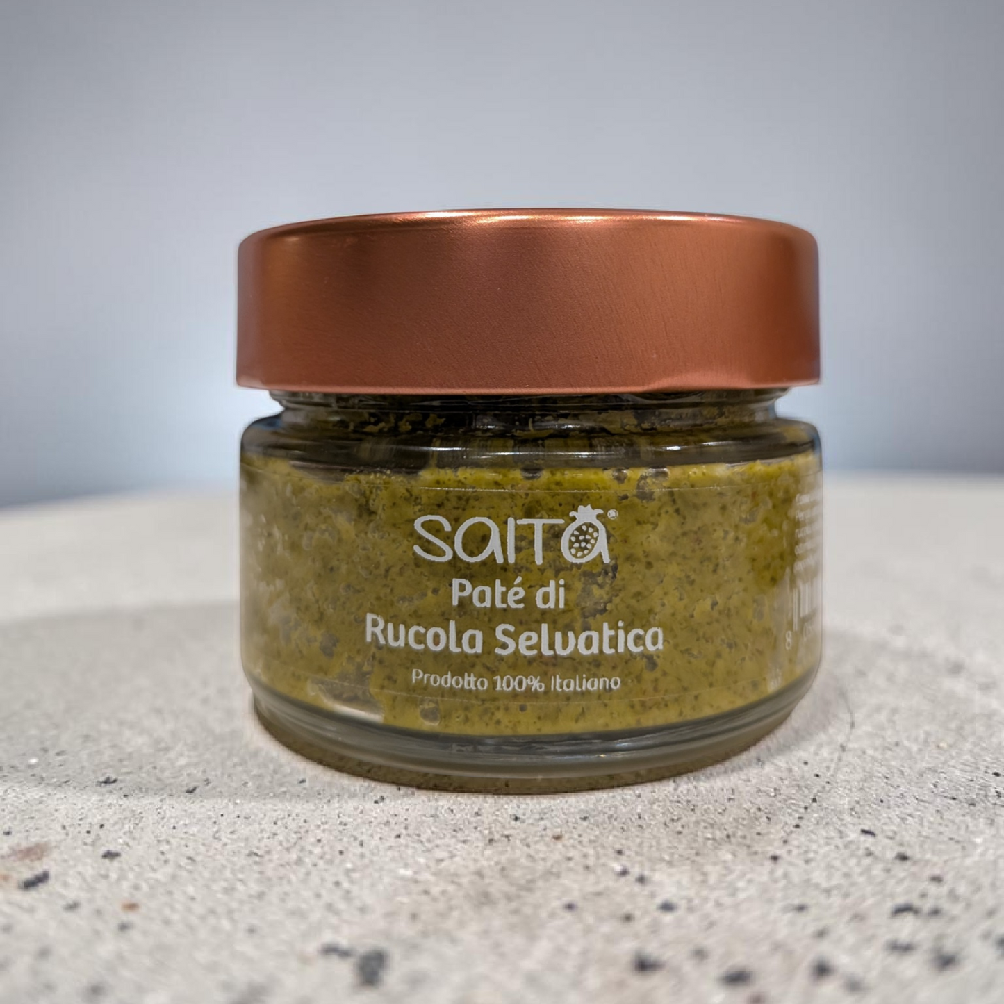 Jar of 'Paté di Rucola Selvatica' with a copper lid on a gray surface.