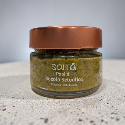 Jar of 'Paté di Rucola Selvatica' with a copper lid on a gray surface.