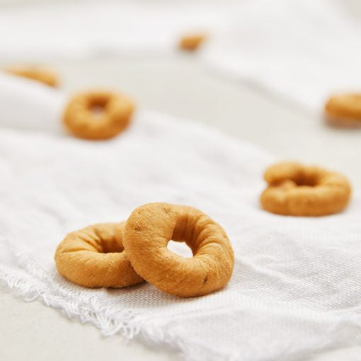 Three golden-brown ring-shaped taralli arranged on a white textured cloth with a soft beige background.