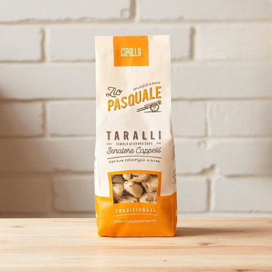 Bag of Zio Pasquale Taralli snacks on a wooden surface with a white stone wall background