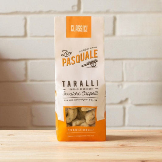Zio Pasquale Taralli snack packaging on a wooden surface with a white stone wall background