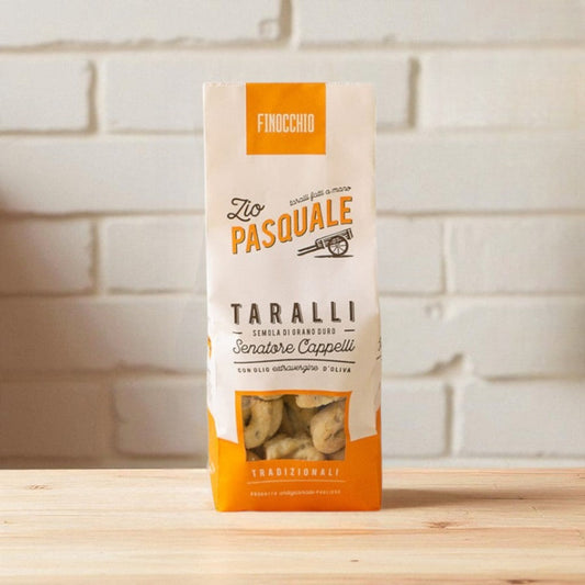 Packaging of Taralli snacks with 'Zio Pasquale' branding on a wooden surface and white stone wall background.