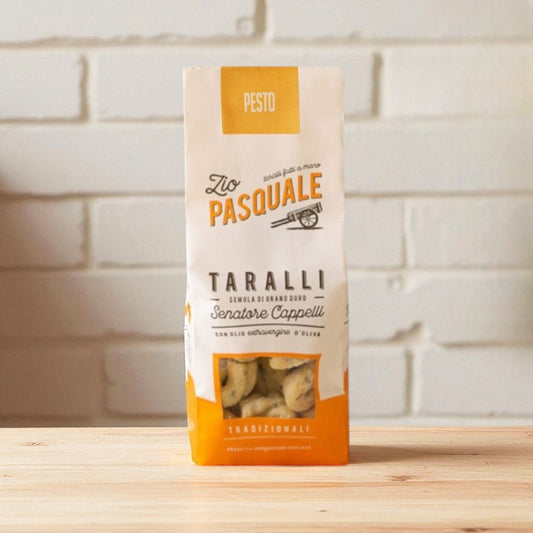 Zio Pasquale Taralli Pesto package on a wooden surface with a white stone wall background