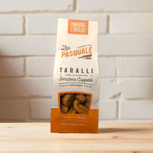 Packaged Taralli snacks on a wooden surface and white stone wall background