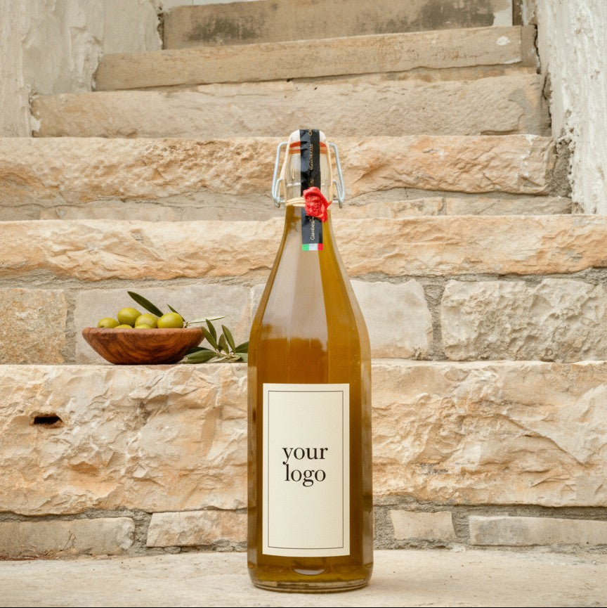 Bottle of wine with a label reading 'your logo' on stone steps with a bowl of olives and leaves.