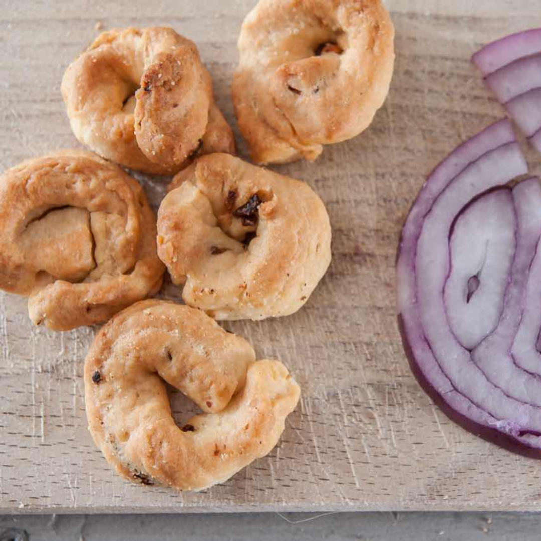 onion flavour taralli on a chopping board with sliced fresh red onion